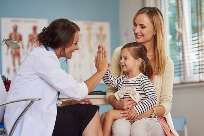 girl sitting in mom's lap giving doctor high five