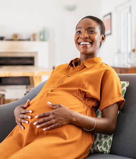 Pregnant woman sitting on a couch with hands on her stomach